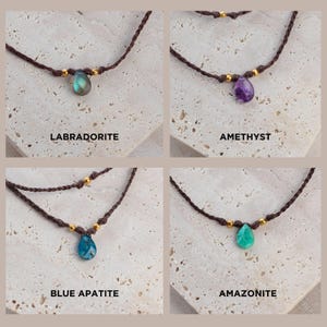 May include: Four necklaces with different gemstone pendants. The necklaces are made of brown cord and have gold beads. The gemstones are labradorite, amethyst, blue apatite, and amazonite.