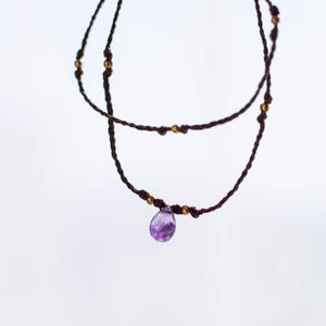 May include: A delicate necklace with a purple amethyst pendant, featuring a brown cord with gold beads.