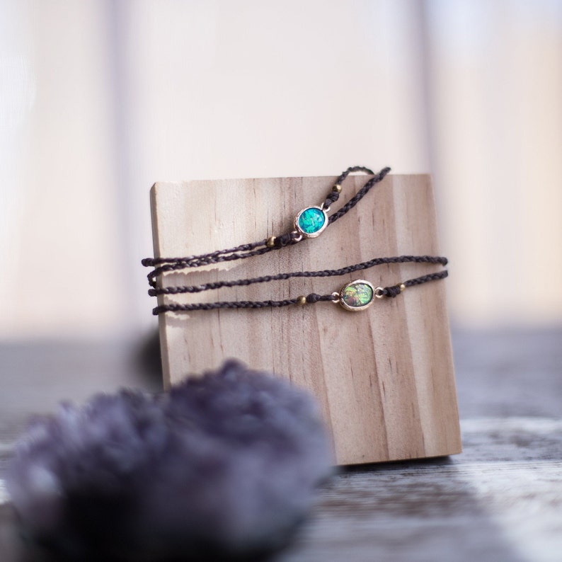 May include: Two layered bracelets with small oval-shaped opal stones. The bracelets are brown and have gold accents. The bracelets are displayed on a wooden block.