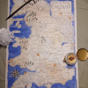 May include: A hand-drawn map of England, with blue and brown ink, showing the text "The Myths and Legends of England." A silver sword and a compass with a gold lid are placed on the map. The map includes the Irish Sea and English Channel.