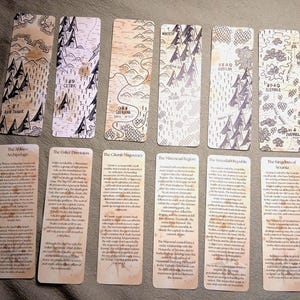 Könnte beinhalten: Eine Sammlung von zwölf rechteckigen Lesezeichen. Jedes Lesezeichen zeigt ein Kartenmuster in Schwarz und Weiß mit Text am unteren Rand. Die Karten zeigen verschiedene Regionen mit Berg- und Baumillustrationen. Die Lesezeichen haben ein Vintage-Aussehen von gealtertem Papier.