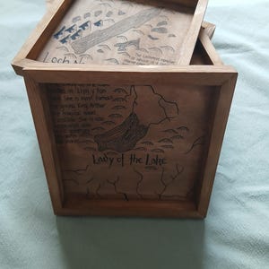 Puede incluir: Bandejas de madera enmarcadas con mapas y texto dibujados a mano. Una bandeja presenta un mapa etiquetado "Loch Ness" con el texto "El monstruo del lago Ness o Nessie es una gran criatura marina." Otra bandeja dice "Lady of the Lake."