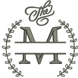 May include: An embroidered design with the word "The" in cursive above a split letter "M", framed by a laurel wreath. The design, in grey tones, is suitable for embroidery projects and customisation.