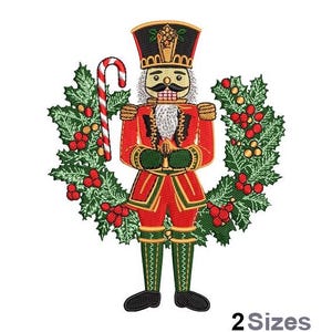 May include: A red and green Christmas wreath with a nutcracker in the centre. The nutcracker is wearing a red and gold uniform and a black hat with a feather. He is holding a candy cane in his right hand.