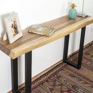 May include: A wooden console table with a live edge top and black metal legs. The table is decorated with a framed photo, a book titled "The World of Coffee", and a pineapple figurine.