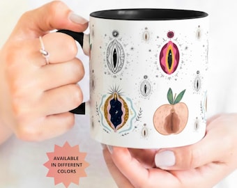 May include: White ceramic mug with a black interior and handle, featuring a repeating pattern of stylized vulva illustrations in various colors. The mug is held by a person. Text on the image reads "AVAILABLE IN DIFFERENT COLORS".