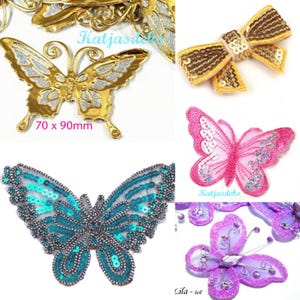 Könnte beinhalten: Eine Sammlung dekorativer Schmetterlings- und Schleifenapplikationen in Gold, Pink, Türkis und Lila mit Pailletten- und Glitzerdetails. Ein goldener Schmetterling ist mit den Maßen 70 x 90mm beschriftet. Text umfasst Katjasdeko und Lila - hell.