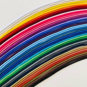May include: A vibrant array of colorful cords, arranged in a rainbow pattern. The cords span a spectrum of hues, including white, yellow, red, pink, purple, blue, green, and brown. The cords are tightly packed and appear to be made of a soft, flexible material.