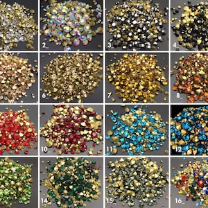 May include: Assortment of 16 different colours of rhinestones, each colour is displayed in a separate pile. The rhinestones are small and have a variety of shapes and sizes.