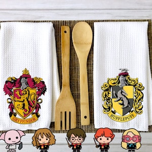 May include: Two white kitchen towels with the Hogwarts house crests for Gryffindor and Hufflepuff. The Gryffindor crest features a lion and the Hufflepuff crest features a badger.  The towels are next to two wooden kitchen utensils.