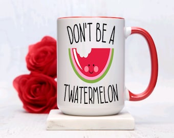 Könnte beinhalten: Weiße Keramiktasse mit rotem Rand und Henkel. Die Tasse hat eine schwarze Grafik mit der Aufschrift "Don't be a twatermelon" mit einer Cartoon-Wassermelone, aus der ein Stück herausgebissen wurde.
