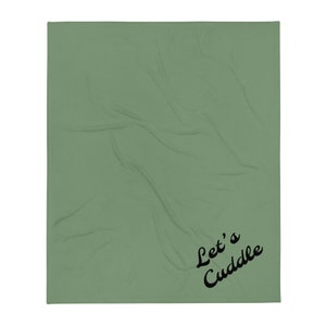 Puede incluir: Una manta de tiro verde salvia con el texto "Let's Cuddle" en letras cursivas negras.