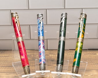 May include: Four pens with different colored patterns and silver tops. The pens are on clear display stands. The tops of the pens feature a silver design of a person playing a sport.