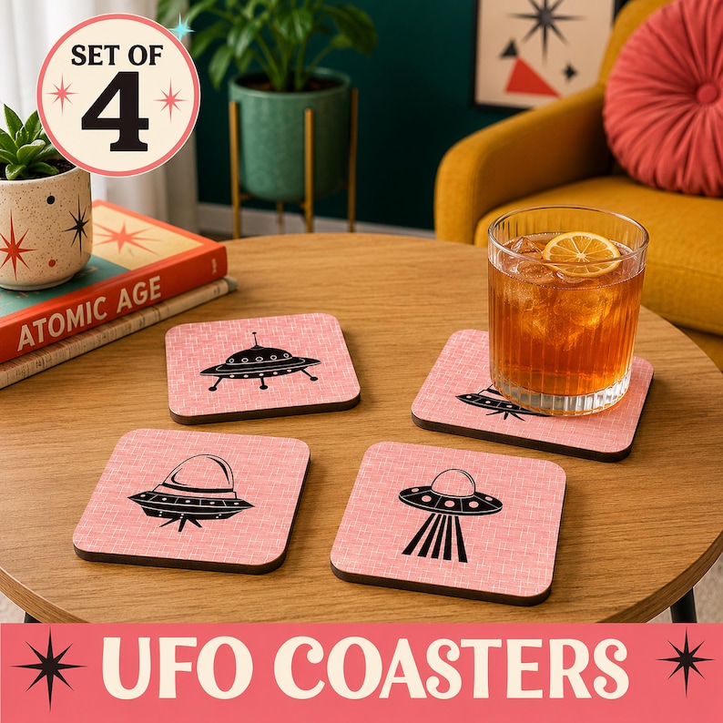 Four square pink coasters with black flying saucer designs, a glass with a drink, and a book on a round wooden table.