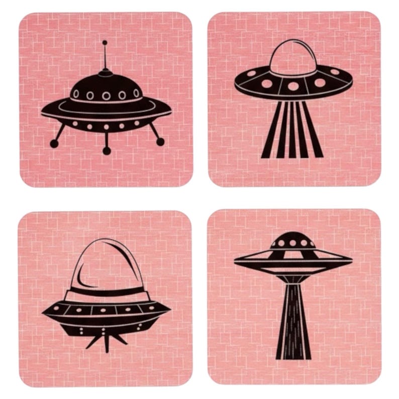 Four square coasters with rounded corners, each featuring a different black UFO illustration on a pink background with a subtle grid pattern.