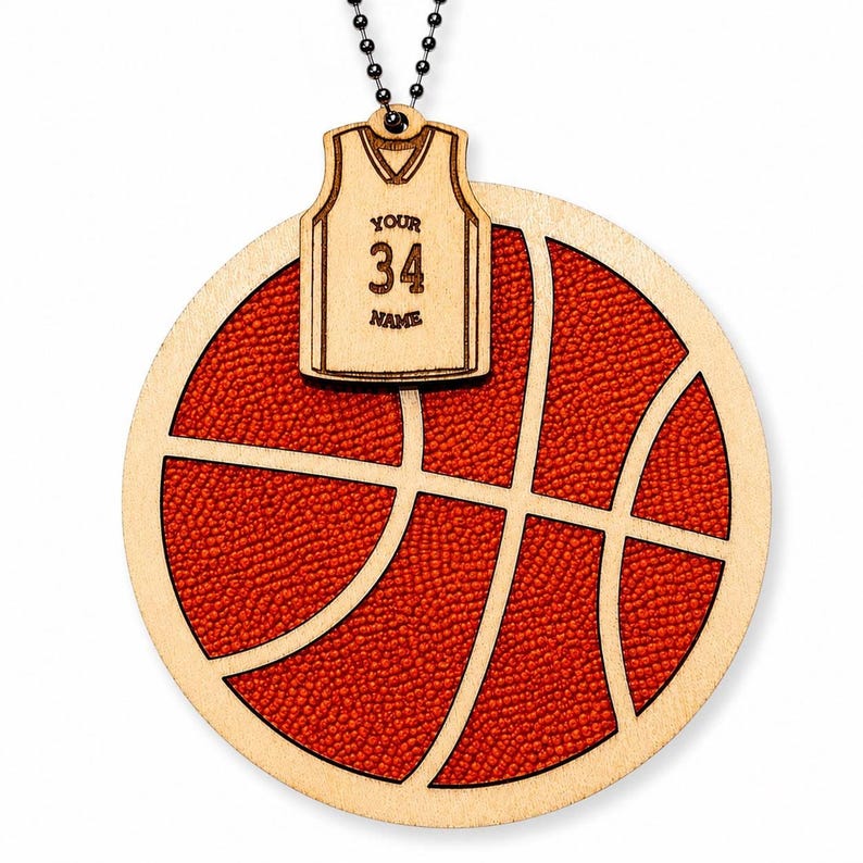 A basketball-shaped wooden ornament with a textured red inlay hangs against a plain white background, joined by a bead chain to a custom jersey plaque.