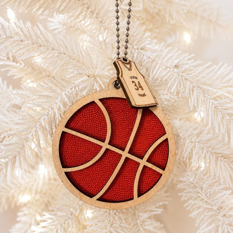 A basketball-shaped wooden ornament with textured orange details hangs in front of a softly lit white artificial Christmas tree.