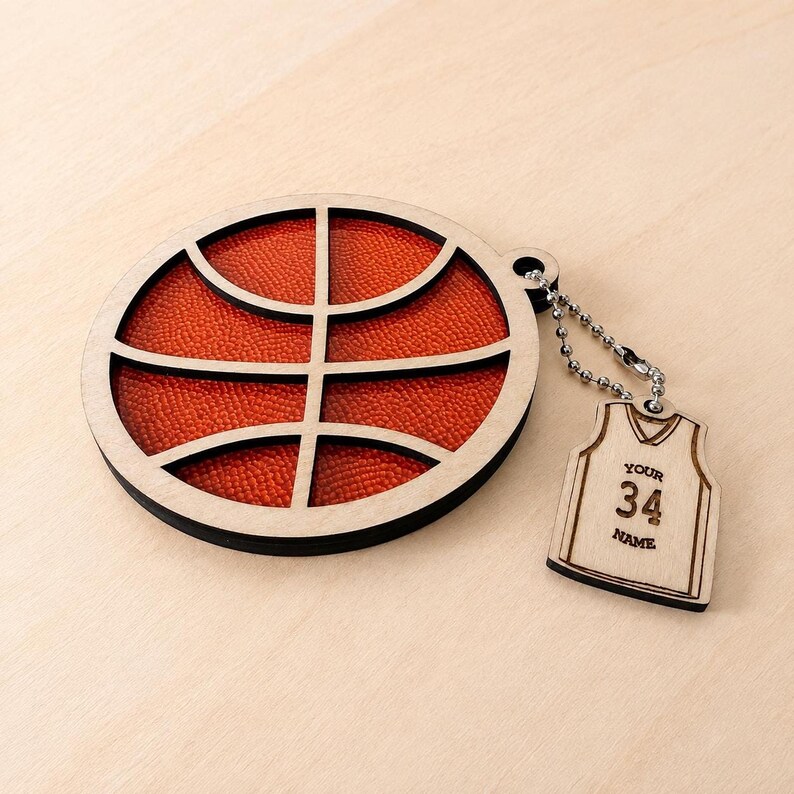 A circular wooden basketball ornament with a textured orange insert lies on a light wooden surface, attached by a chain to a jersey-shaped wooden tag.