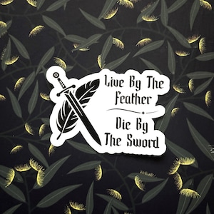 Op de afbeelding: Een witte sticker met de tekst "Live By The Feather Die By The Sword" in een gotisch lettertype. De sticker heeft een zwart zwaard en een veermotief. De achtergrond is een donker patroon van bladeren en gele accenten.