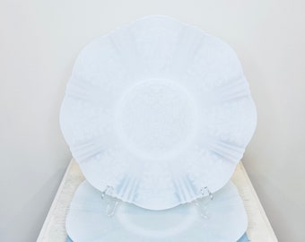 Può includere: Due piatti da portata in ceramica bianchi e a forma di conchiglia impilati uno sopra l'altro. I piatti hanno un design delicato in rilievo.