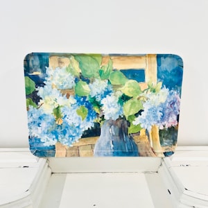 May include: A rectangular serving tray featuring a watercolor painting of blue and white hydrangea flowers in a vase. The artwork depicts lush green leaves and soft floral clusters set against a wooden chair background with deep blue accents.
