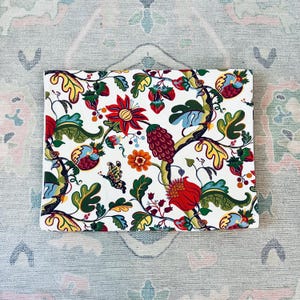May include: A rectangular fabric piece featuring a white background with a dense, colorful botanical pattern. The design includes stylized red, orange, and yellow flowers, green leaves, dark red berries, and a small butterfly scattered throughout.