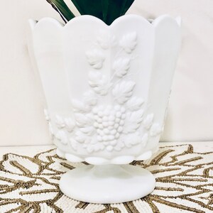 May include: White milk glass planter with a grapevine design. The planter has a scalloped rim and a pedestal base.