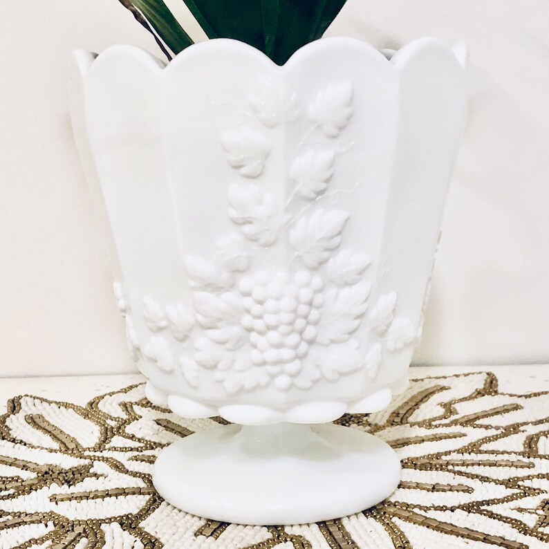 May include: White milk glass planter with a grapevine design. The planter has a scalloped rim and a pedestal base.