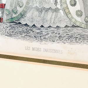 K&ouml;nnte beinhalten: Eine Schwarzwei&szlig;illustration einer Frau in einem Kleid mit Spitzenbesatz. Das Kleid hat einen gr&uuml;n-wei&szlig; karierten Muster auf dem Rock. Das Bild tr&auml;gt den Titel "LES MODES PARISIENNES".
