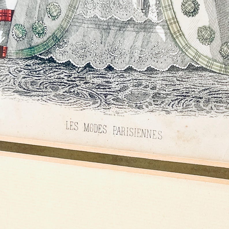 K&ouml;nnte beinhalten: Eine Schwarzwei&szlig;illustration einer Frau in einem Kleid mit Spitzenbesatz. Das Kleid hat einen gr&uuml;n-wei&szlig; karierten Muster auf dem Rock. Das Bild tr&auml;gt den Titel "LES MODES PARISIENNES".