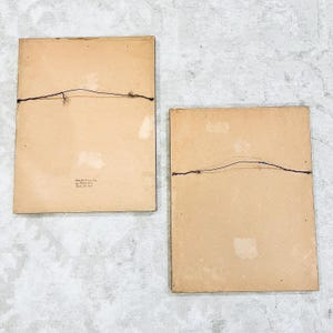 K&ouml;nnte beinhalten: Zwei braune Bilderrahmen mit einem einfachen schwarzen Draht-Aufh&auml;ngesystem auf der R&uuml;ckseite. Die Rahmen sind beide rechteckig und haben eine hellbraune Pappe als R&uuml;ckwand.