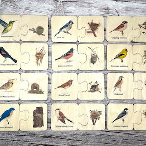 May include: Wooden puzzle set featuring colorful illustrations of various bird species, including a hummingbird, blue jay, and chipping sparrow. Each puzzle piece depicts a bird and its nest, designed for educational play. The set includes 16 pieces.