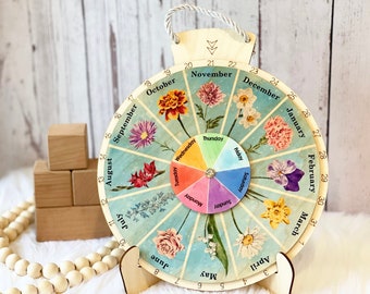 May include: A circular wooden perpetual calendar featuring a floral design with twelve months labeled around the perimeter and a central rotating wheel displaying the days of the week. The calendar includes numbers 1 through 31 and a rope hanger.