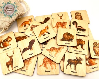 May include: A collection of square wooden tiles featuring illustrations of North American wildlife including a red fox, beaver, skunk, chipmunk, deer, eagle, coyote, brown bear, cougar, and moose, each labeled with its name, accompanied by a drawstring bag.