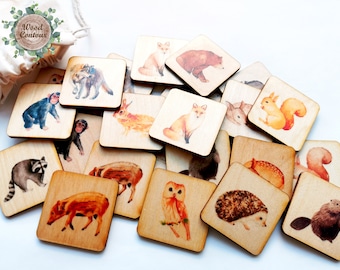 May include: A collection of square wooden tiles featuring watercolor illustrations of various forest animals including a fox, bear, squirrel, owl, hedgehog, beaver, raccoon, and monkey, accompanied by a small drawstring storage bag.
