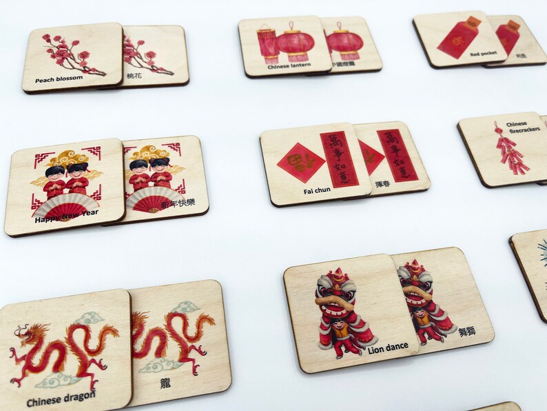 May include: A set of square wooden tiles featuring illustrations related to Chinese New Year, including peach blossoms, lanterns, red pockets, firecrackers, dragons, lion dances, and figures with text labels in English and Chinese characters.