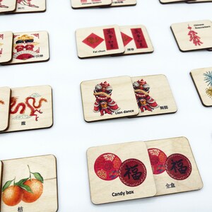 May include: A collection of square wooden tiles featuring colorful illustrations and text related to Chinese New Year traditions, including a lion dance, Chinese dragon, fireworks, candy box, and tangerines, with English and Chinese labels.