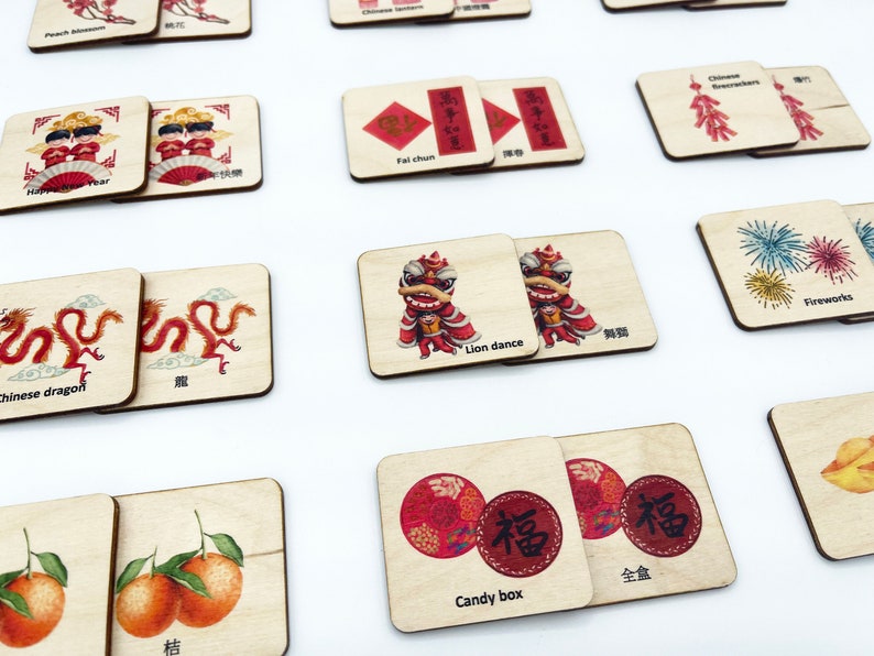 May include: A collection of square wooden tiles featuring colorful illustrations and text related to Chinese New Year traditions, including a lion dance, Chinese dragon, fireworks, candy box, and tangerines, with English and Chinese labels.