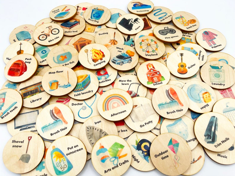 May include: A collection of 36 round wooden tokens with various images and text. The tokens are painted with watercolor illustrations of activities, chores, and routines. Some of the text on the tokens includes 'Brush Hair', 'Mow the Lawn', 'Camping', 'School', 'Guitar', 'Playland', 'Take a Bath', 'Put on Sunscreen', 'Arts and Crafts', 'Night', 'Outdoor Time', 'Trim Nails', 'Music', 'Laundry', 'Go Potty', 'Iron', 'Afternoon', 'Fold Laundry', 'Doctor', 'Library', 'Shovel Snow', 'Pack Bag', 'Make Bed', 'Bike Ride', 'Dusting', 'Swimming', 'Walk the Dog', 'Snack Time', 'School Trip', 'Play Games', 'Pajamas', 'Wash Car', 'Activities', 'Map Floor', '4 the Fish', 'Brush Teeth', 'Pack Bag', 'Take a Bath'.