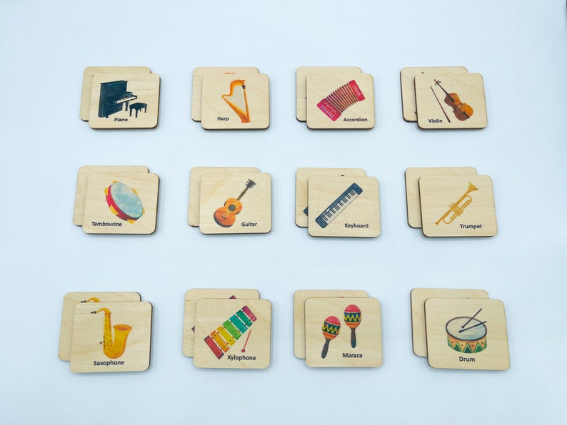 May include: A set of twelve square wooden tiles featuring colorful illustrations of musical instruments including a piano, harp, accordion, violin, tambourine, guitar, keyboard, trumpet, saxophone, xylophone, maracas, and a drum with labels.