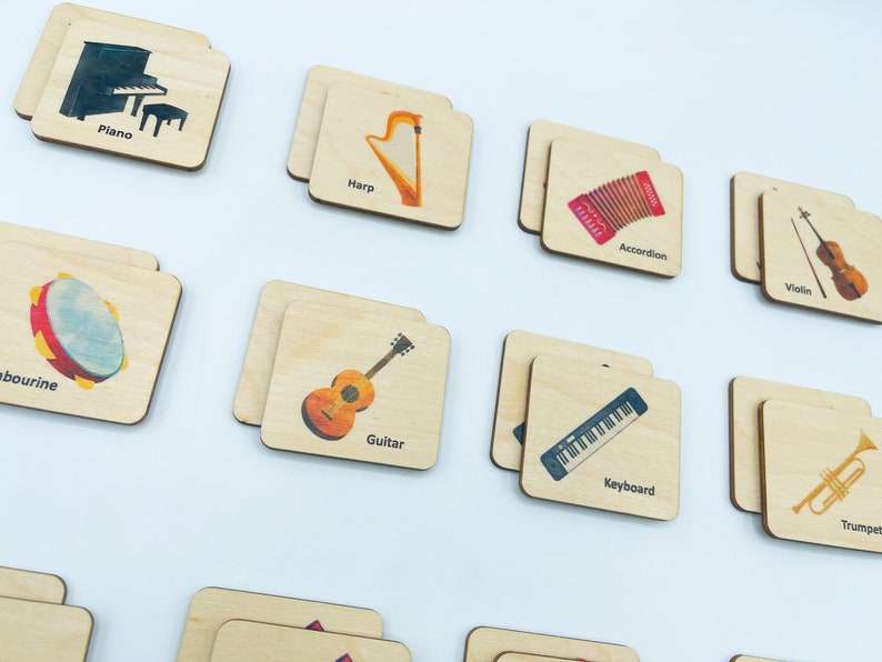 May include: A collection of rectangular wooden tiles featuring colorful illustrations of musical instruments including a piano, harp, accordion, violin, tambourine, guitar, keyboard, and trumpet, each labeled with its corresponding name in black text.