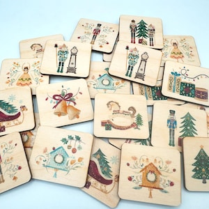 May include: A collection of square wooden tiles featuring various Christmas-themed illustrations including nutcrackers, ballerinas, sleighs, rocking horses, birdhouses, and gift boxes, all rendered in a soft, watercolour-style colour palette.