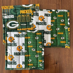 Op de afbeelding: Set van vier groene en witte gequilte ovenwanten met het logo van de Green Bay Packers en de woorden "Packers" en "Go Pack Go".