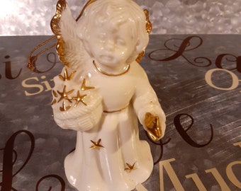 May include: A white porcelain angel ornament with gold accents. The angel is holding a basket of gold stars.