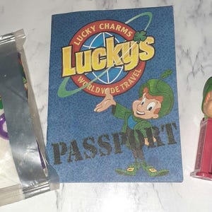 May include: A blue and white passport-style card with the text "Lucky Charms Lucky's Worldwide Travel Passport". A cartoon leprechaun character is holding a green shamrock. A small plastic toy of the leprechaun is also included.