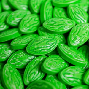 Puede incluir: Primer plano de un mont&oacute;n de caramelos verdes brillantes. Cada caramelo tiene forma ovalada con un dise&ntilde;o blanco y arremolinado en la superficie. Los caramelos son brillantes y parecen caramelos duros o pastillas.
