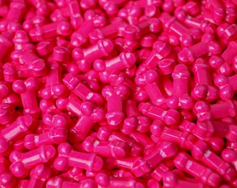 May include: A large collection of small, bright pink, phallus-shaped candies. Each individual piece features a rounded top and a cylindrical base, creating a uniform, repetitive pattern across the entire frame with a vibrant, solid color.
