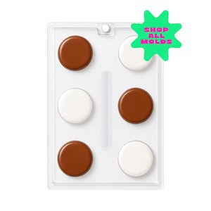 May include: A clear plastic mold containing six round, chocolate-colored and white candies. The candies are arranged in a rectangular pattern. A green star-shaped graphic with the text "SHOP ALL MOLDS" is in the upper right corner.