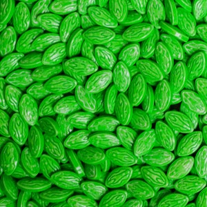 Puede incluir: Primer plano de un mont&oacute;n de caramelos verdes brillantes en forma ovalada. Cada caramelo tiene un patr&oacute;n texturizado, similar a una sand&iacute;a. Los caramelos son brillantes y est&aacute;n distribuidos uniformemente, llenando el encuadre.