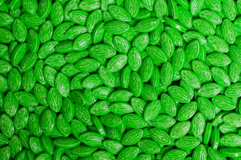 Puede incluir: Primer plano de un mont&oacute;n de caramelos verdes brillantes en forma ovalada. Cada caramelo tiene un patr&oacute;n texturizado, similar a una sand&iacute;a. Los caramelos son brillantes y est&aacute;n distribuidos uniformemente, llenando el encuadre.
